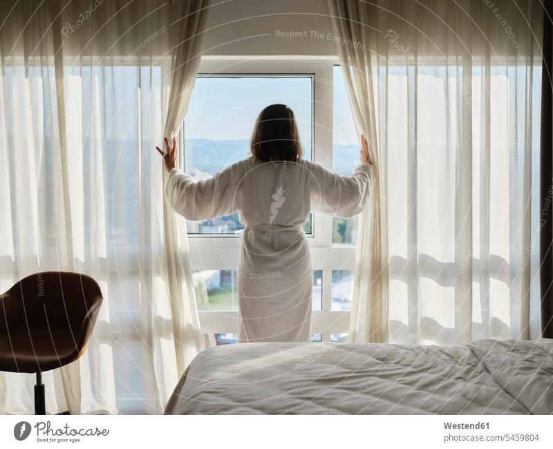 Woman opening white curtain while looking through window at luxury hotel room color image colour image indoors indoor shot indoor shots interior interior view