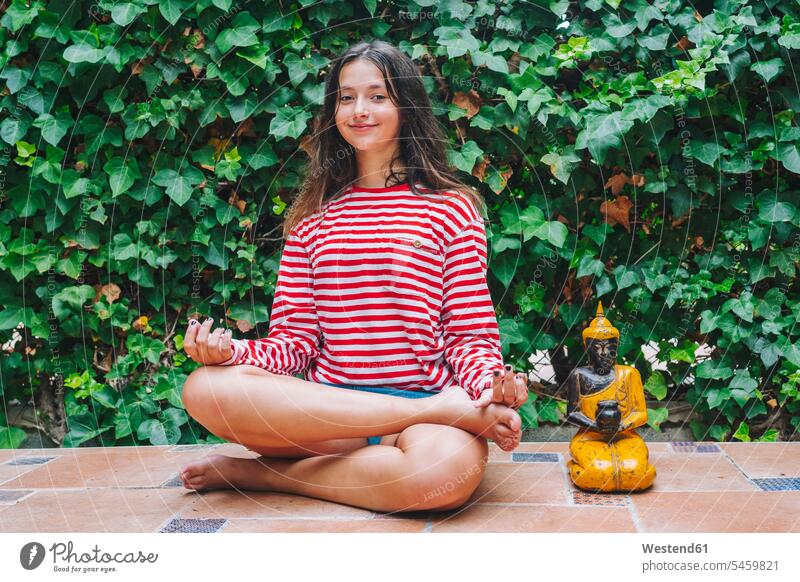 Smiling girl meditating by Buddha sculpture in backyard color image colour image outdoors location shots outdoor shot outdoor shots day daylight shot