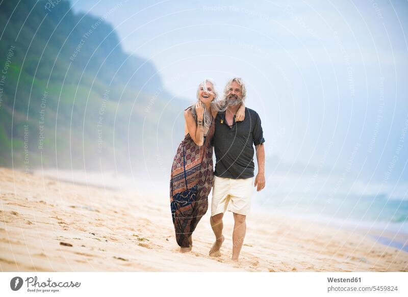 Happy senior hippie couple strolling side by side on the beach beaches happiness happy paralell Juxtaposed in paralell walking taking a walk take a walk Hippy
