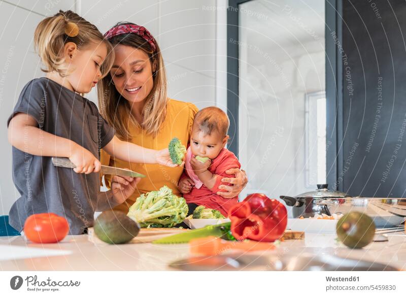 Mother holding baby girl while guiding daughter in cutting vegetables on kitchen island color image colour image indoors indoor shot indoor shots interior