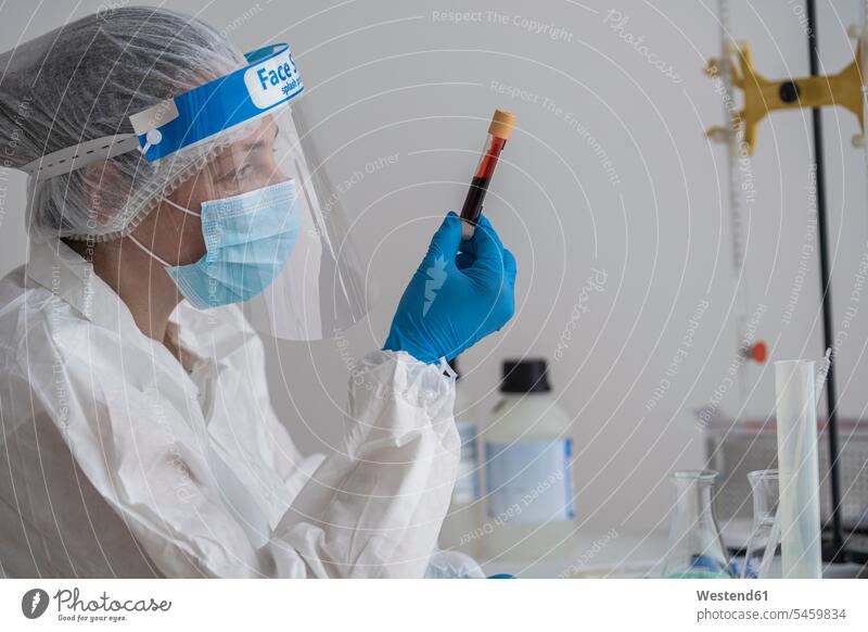 Woman in protective wear sitting at desk examining blood sample Occupation Work job jobs profession professional occupation Tables desks At Work hold health