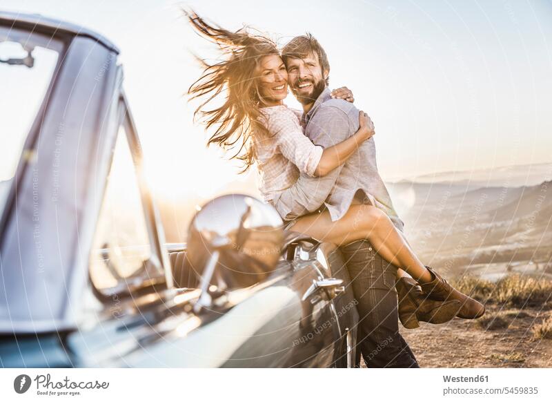Happy couple at convertible car in the countryside at sunset touristic tourists shirts motor vehicles road vehicle road vehicles Auto automobile Automobiles