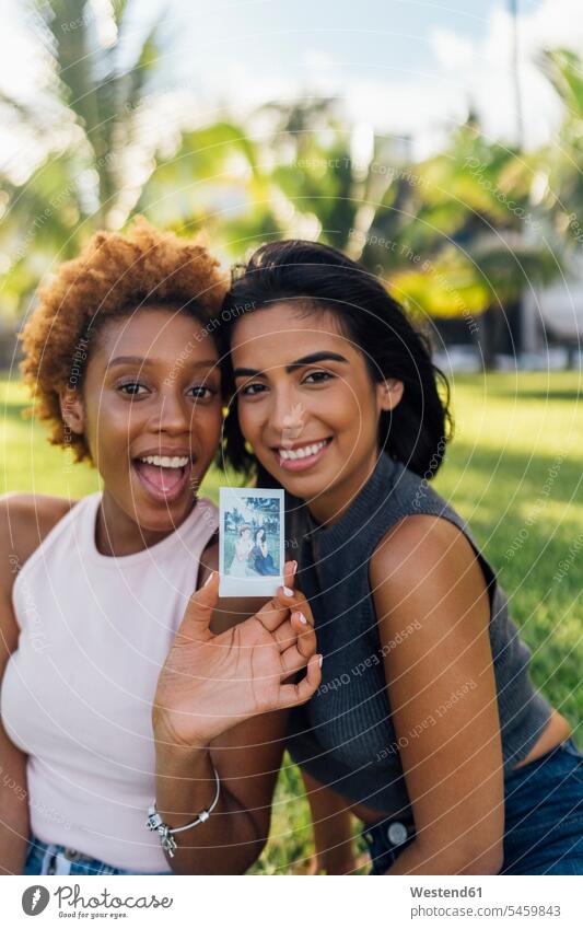 Two happy female friends showing an instant photo in a park happiness instant photography polaroid polaroids instant photos Showing photographs relaxed