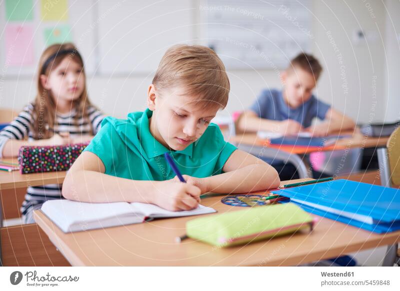 Schoolboy writing in exercise book in class write Exercise Book Workbook Schoolboys school class schools booklet booklets notebooks three people 3