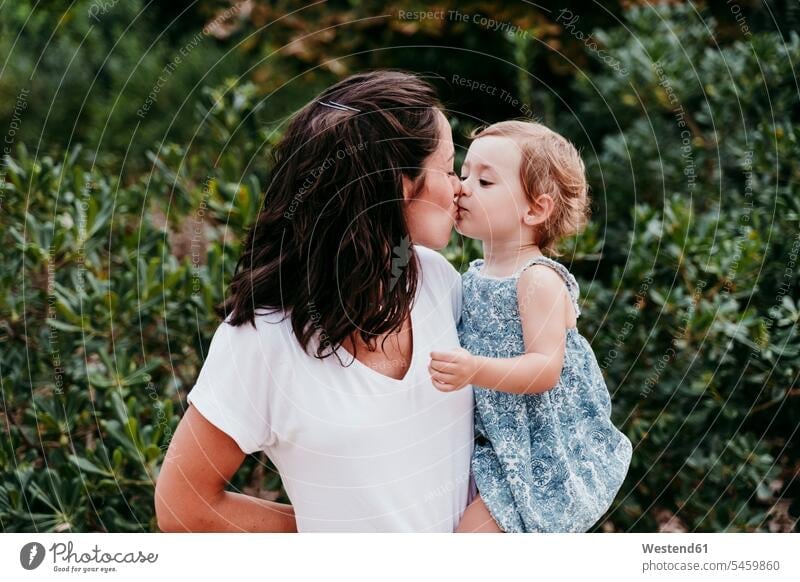 Happy mother and daughter kissing each other while standing in park color image colour image outdoors location shots outdoor shot outdoor shots day