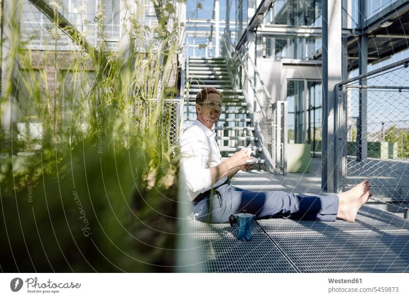 Male professional with coffee relaxing on floor in plant nursery color image colour image Germany business people businesspeople Business Professional