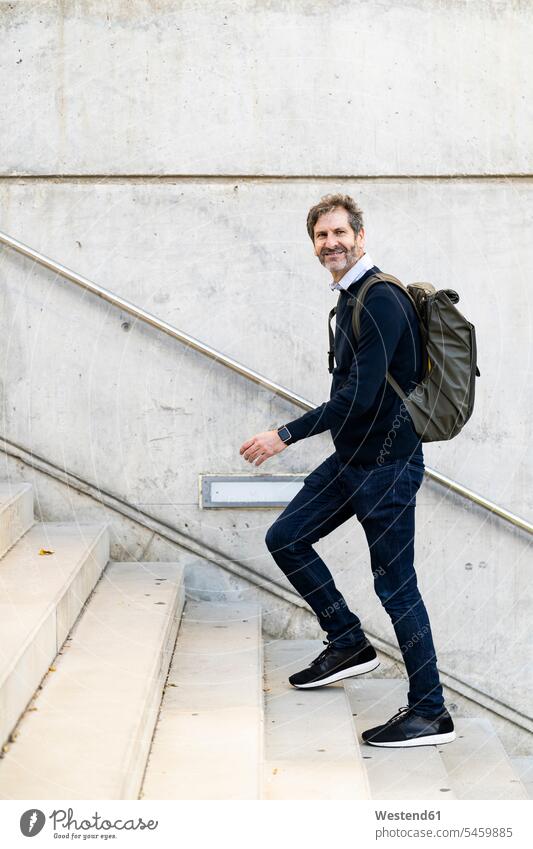 Smiling mature man with a backpack walking up stairs in the city rucksacks backpacks back-packs men males upstairs town cities towns smiling smile stairway
