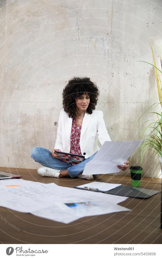 Businesswoman sitting on the floor in a loft working with tablet and documents businesswoman businesswomen business woman business women lofts floors Seated