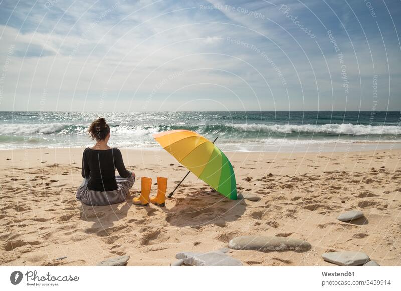 Woman with colorful umbrella sitting on the beach, rear view Wellington Boot rubber boots Gumboots Rubber Boot wellies Wellington Boots wellingtons sunbathing