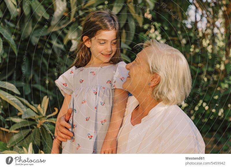 Smiling senior woman looking at cute granddaughter against plants in yard color image colour image Spain leisure activity leisure activities free time