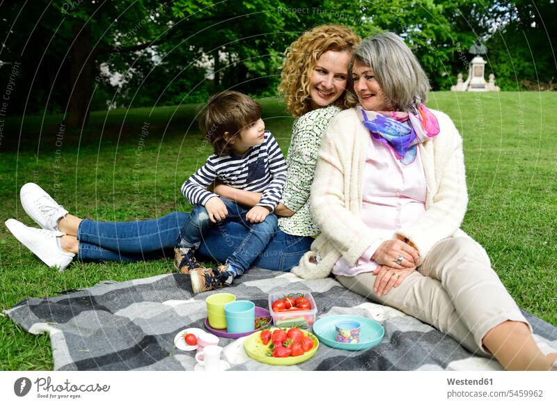 Happy boy enjoying picnic with mother and grandmother at public park color image colour image outdoors location shots outdoor shot outdoor shots day