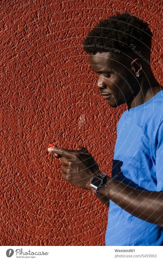 Close-up of young man using smart phone against red wall in city during sunny day color image colour image Spain leisure activity leisure activities free time