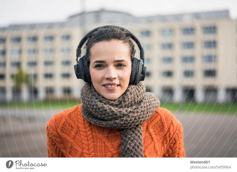Portrait of smiling woman wearing scarf and orange knit pullover listening music with headphones knit sweater Cardigan Sweater hearing females women portrait