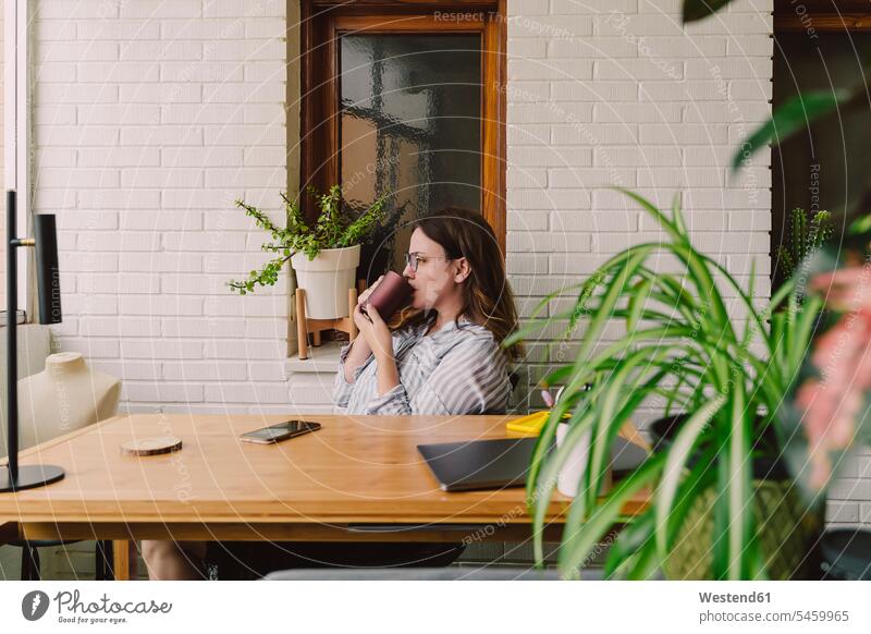 Thoughtful woman drinking coffee while sitting at desk in home office color image colour image indoors indoor shot indoor shots interior interior view Interiors