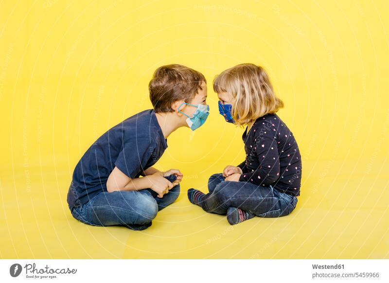 Side view of siblings sitting face to face against yellow background color image colour image coloured background colored background studio shot
