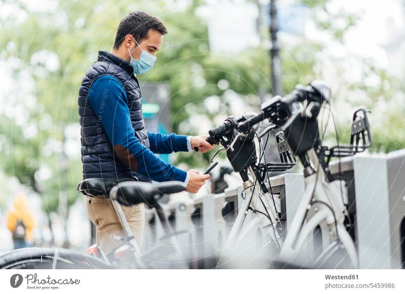 Young man using smart phone at bicycle parking station during coronavirus color image colour image outdoors location shots outdoor shot outdoor shots day