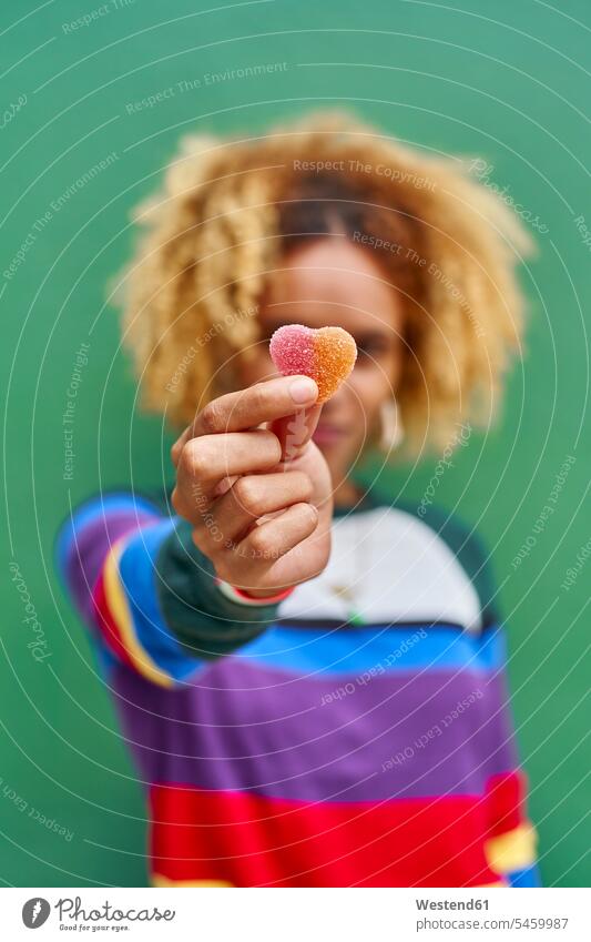 Young woman holding candy heart while standing against green wall color image colour image Mozambique Africa outdoors location shots outdoor shot outdoor shots