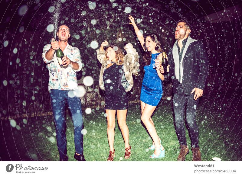 Young man opening champagne while friends dancing outdoors in party at night color image colour image leisure activity leisure activities free time leisure time