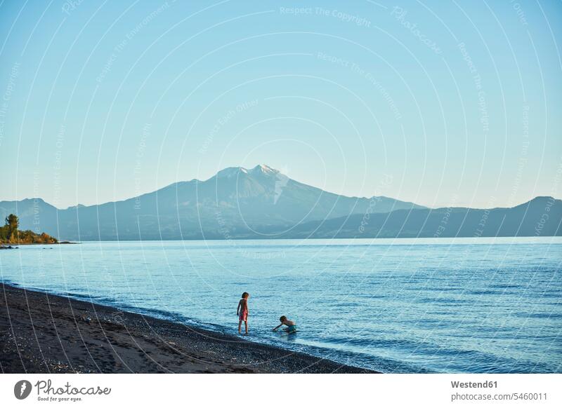 Chile, Lago Llanquihue, Calbuco volcano, two boys playing in water lake lakes males waters body of water child children kid kids people persons human being