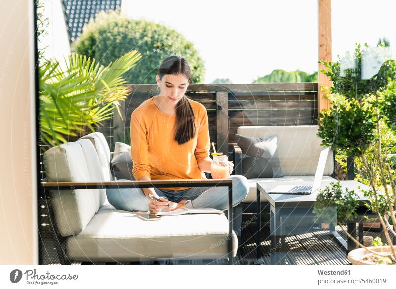Young woman sitting on couch on terrace with healthy drink and notebook human human being human beings humans person persons caucasian appearance