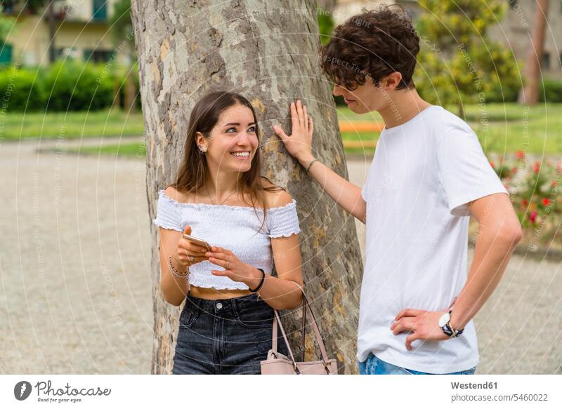 Young couple in a park, woman showing him her smartphone and smiling telecommunication phones telephone telephones cell phone cell phones Cellphone mobile