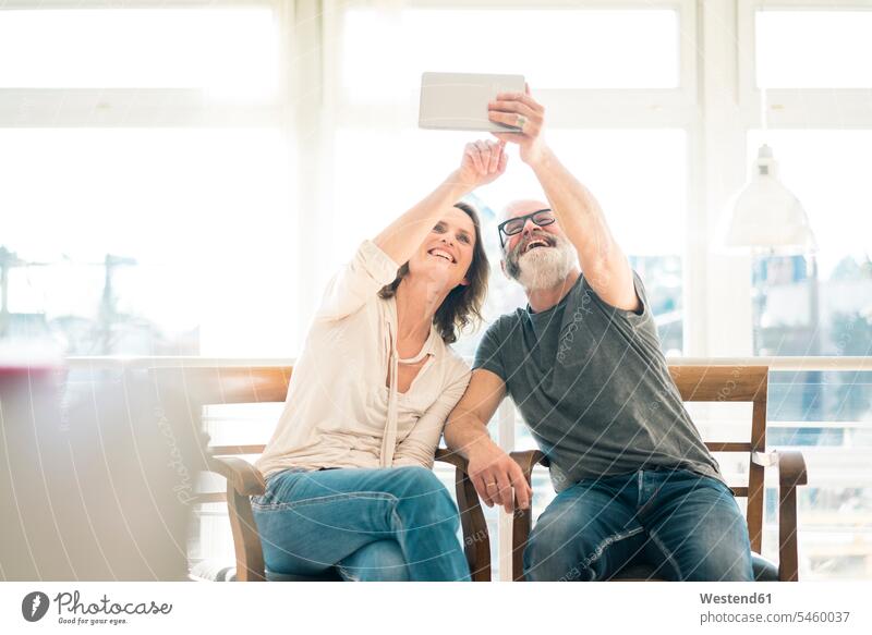 Happy mature couple sitting on chairs at home using tablet twosomes partnership couples Seated Joy enjoyment pleasure Pleasant delight digitizer Tablet Computer