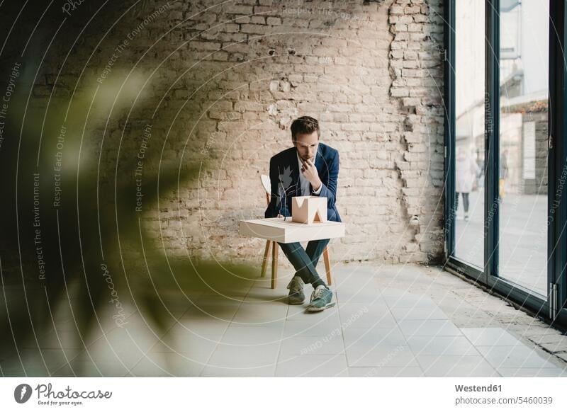Businessman sitting at brick wall looking at architectural model human human being human beings humans person persons caucasian appearance caucasian ethnicity