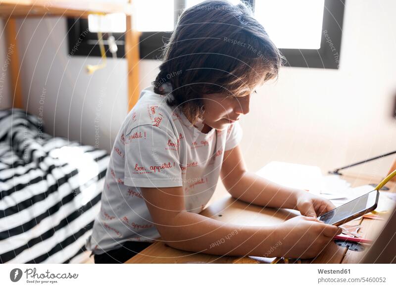 Boy sitting at desk at home using smartphone T- Shirt t-shirts tee-shirt Tables desks telecommunication phones telephone telephones cell phone cell phones