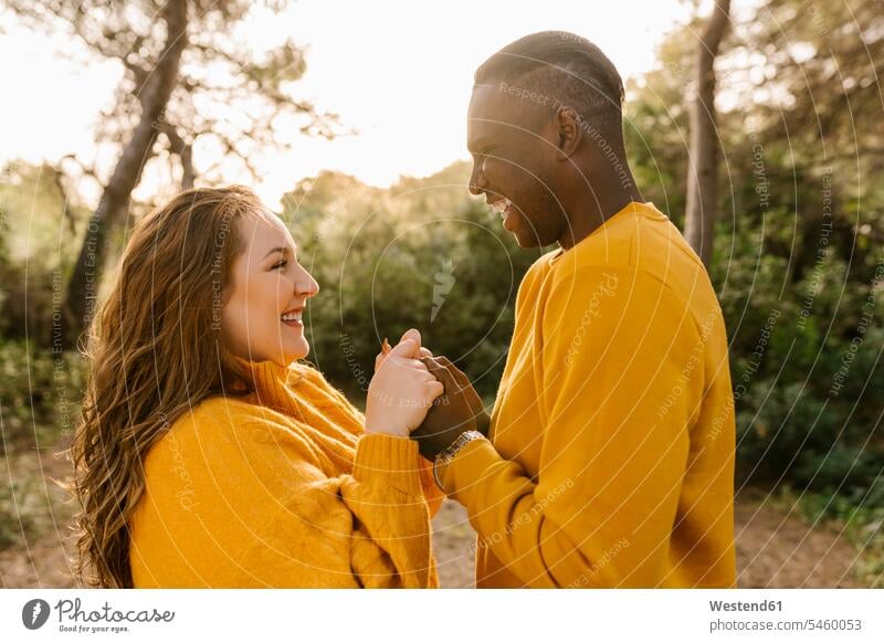 Happy couple holding hands while standing at forest color image colour image outdoors location shots outdoor shot outdoor shots Spain casual clothing