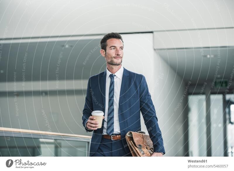 Businessman with briefcase walking in office building, holding cup of coffee Success successful suit Fullsuit suits full suit Business man Businessmen