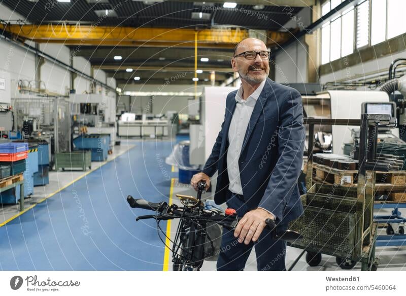 Smiling businessman with bicycle in a factory Occupation Work job jobs profession professional occupation business life business world business person