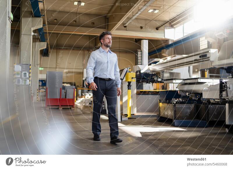 Businessman looking at manufacturing machine while walking at factory color image colour image indoors indoor shot indoor shots interior interior view Interiors