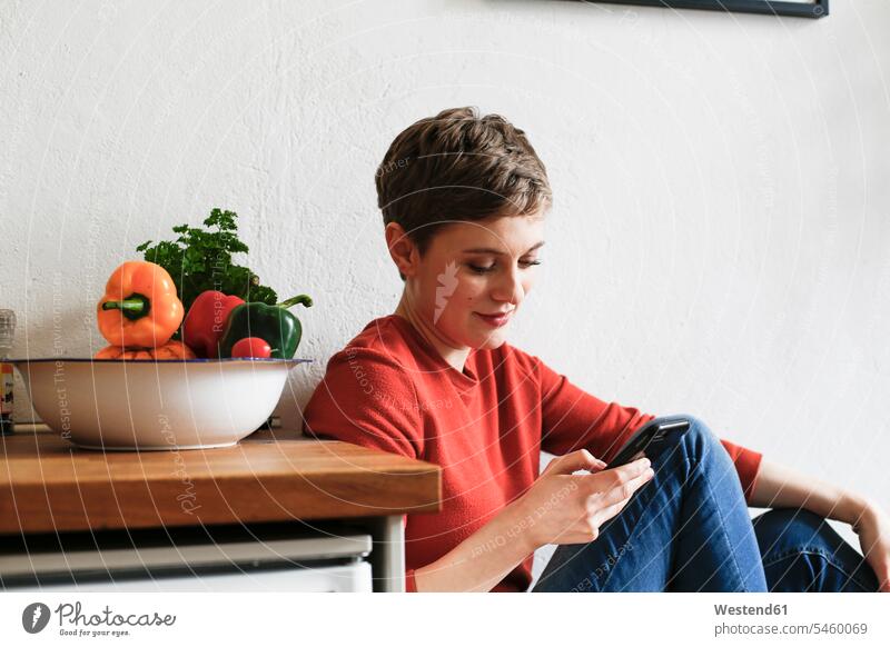 Woman sitting in kitchen, checking smartphone messages domestic kitchen kitchens texting sending text messaging SMS Text Message Smartphone iPhone Smartphones