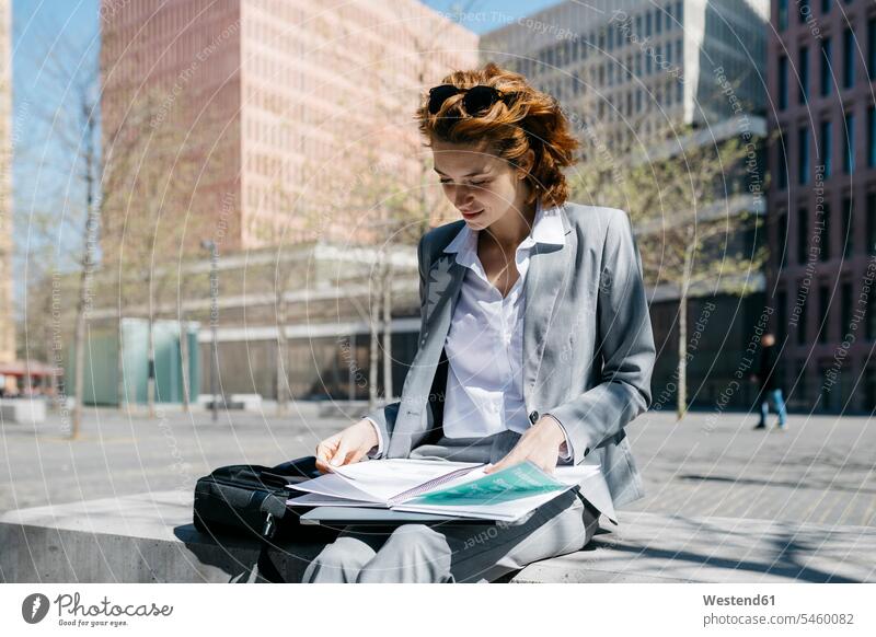 Young businesswoman reading documents, sitting on a bench in the city on a sunny day pantsuit trouser suit Pant Suit urban urbanity Seated working At Work