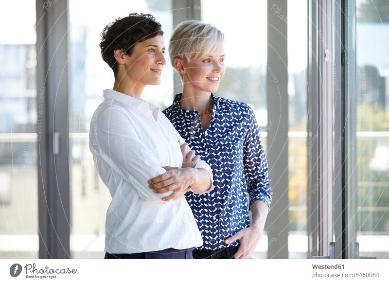 Two smiling businesswomen looking out of window in office windows portrait portraits businesswoman business woman business women smile offices office room