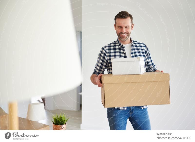 Happy man moving into new flat carrying cardboard box happiness happy men males flats apartment apartments move in cardboard boxes packing case packing cases