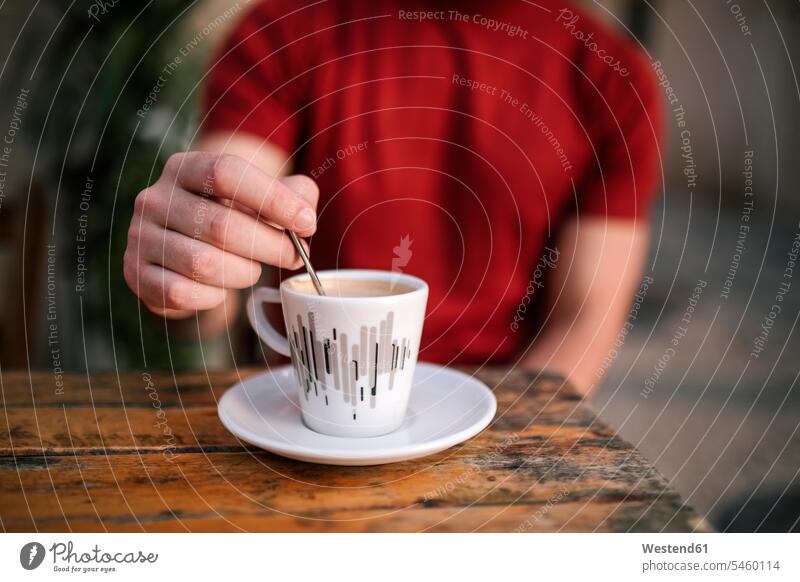 Close-up of man’s hand stirring coffee while sitting at sidewalk cafe color image colour image outdoors location shots outdoor shot outdoor shots day