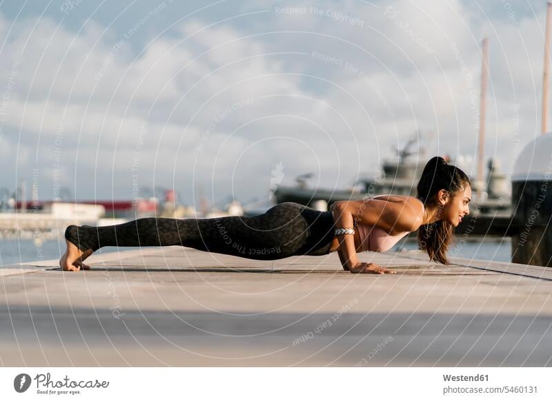 Female athlete practicing four-limbed staff pose on pier at harbor color image colour image Spain outdoors location shots outdoor shot outdoor shots day