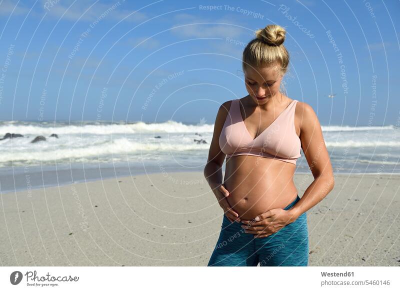 Active pregnant woman on the beach touching her belly bellies stomach stomachs Pregnant Woman portrait portraits females women active beaches upper body