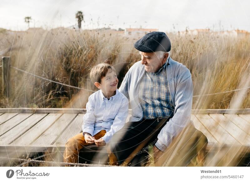 Grandfather sitting with his grandson on boardwalk talking communication Grass Grasses close closeness propinquity assistance Looking After support care Care
