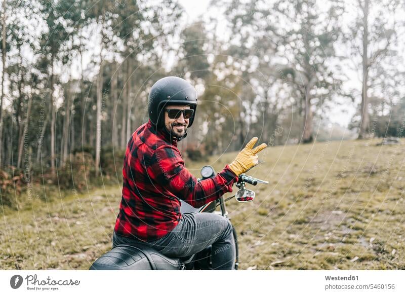 Smiling male biker gesturing while exploring forest on motorcycle color image colour image Spain outdoors location shots outdoor shot outdoor shots day