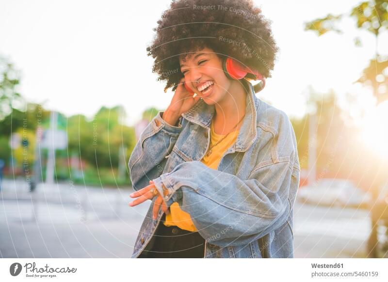Happy young woman with afro hairdo dancing in the city human human being human beings humans person persons curl curled curls curly hair jewelry headphone