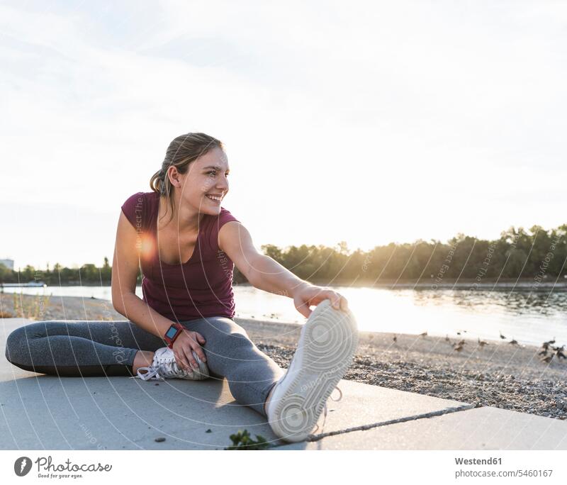 Young woman sitting on ground at the river, warming up for training fitness stretching warm up Sitting On The Floor Sitting On Floor sport sports full length