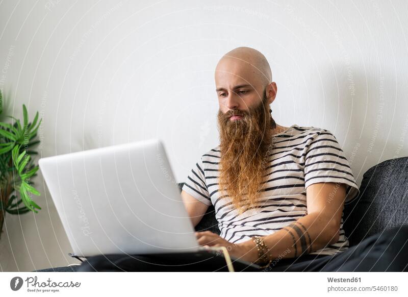 Portrait of hipster using laptop at home mobile working tattooed individuality Distinct looking down casual leisure wear casual clothing casual wear