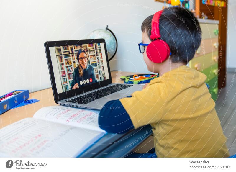 Boy listening to teacher through headphones during video call at home color image colour image indoors indoor shot indoor shots interior interior view Interiors