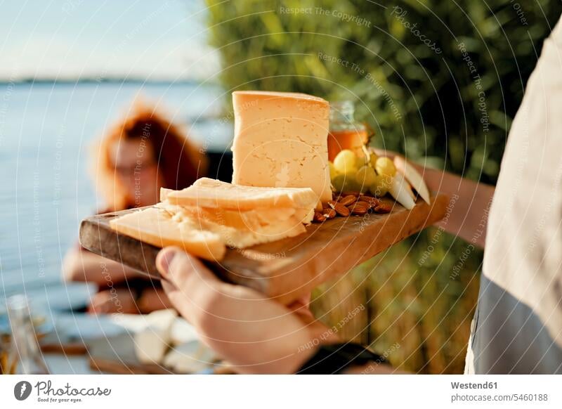 Man serving cheese platter for friends at a lake human human being human beings humans person persons caucasian appearance caucasian ethnicity european 2
