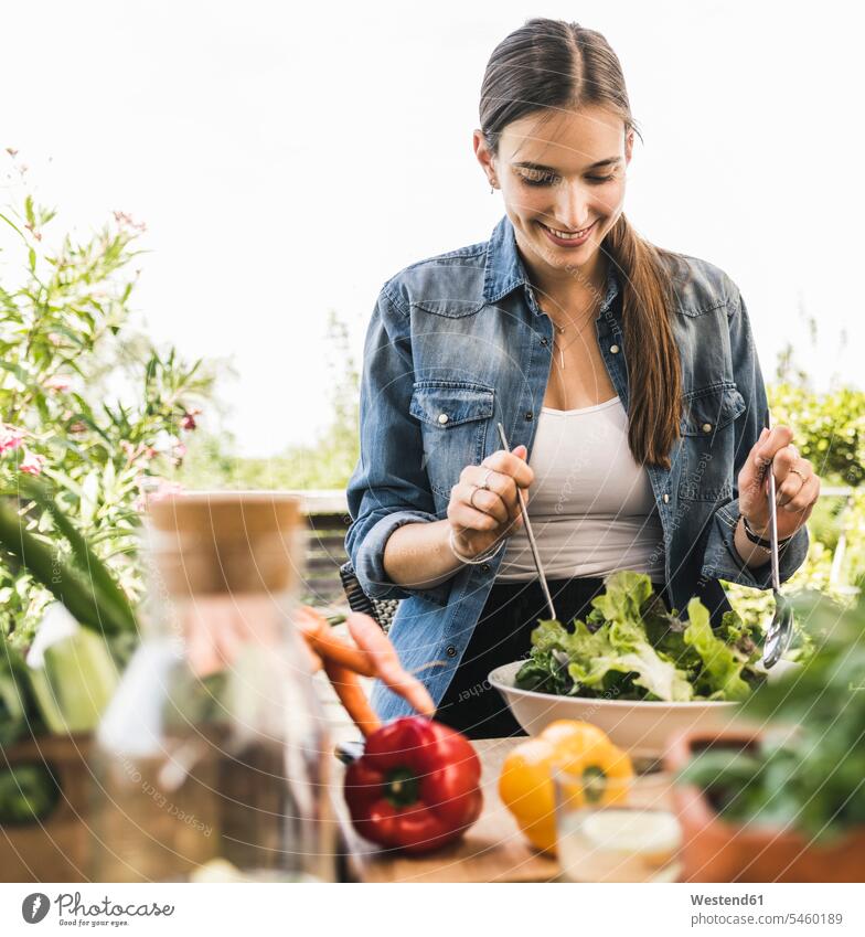 Smiling young woman making salad in bowl while sitting against clear sky at yard color image colour image Germany leisure activity leisure activities free time