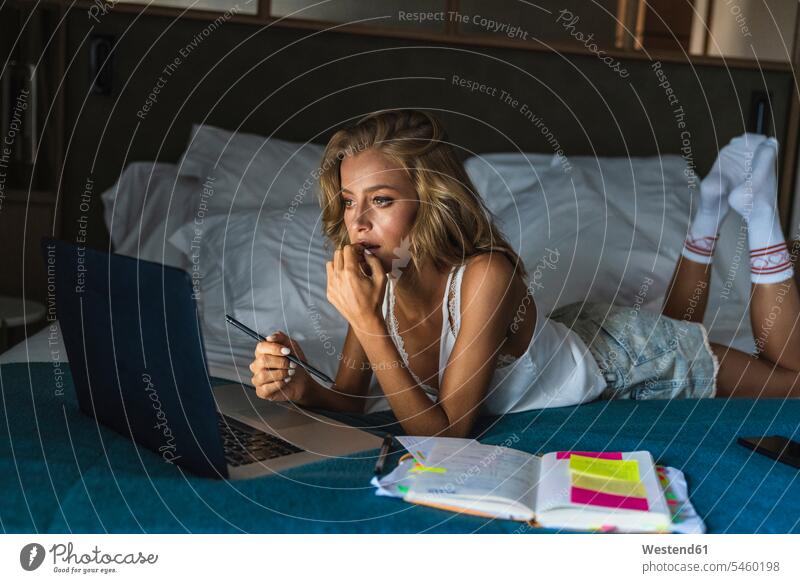 Woman lying on bed, using laptop hotel room hotel rooms hotelroom beds blond blond hair blonde hair using a laptop Using Laptops Laptop Computers laptops