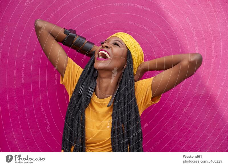 Portrait of woman with long dreadlocks laughing in front of a pink wall caps hat hats T- Shirt t-shirts tee-shirt smile delight enjoyment Pleasant pleasure