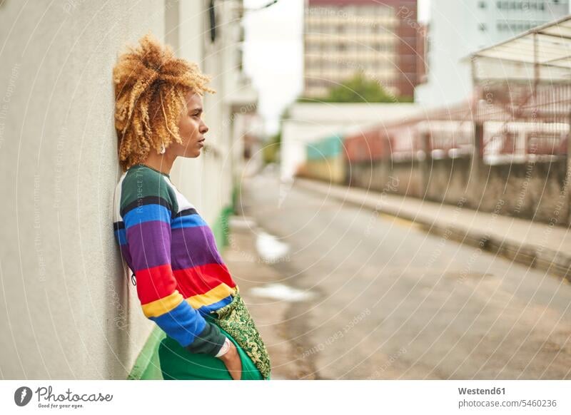 Portrait of a young woman in an afro hairstyle leaning on a wall in the city bags wait contemplative pensively Reflective thoughtful stand Distinct individual